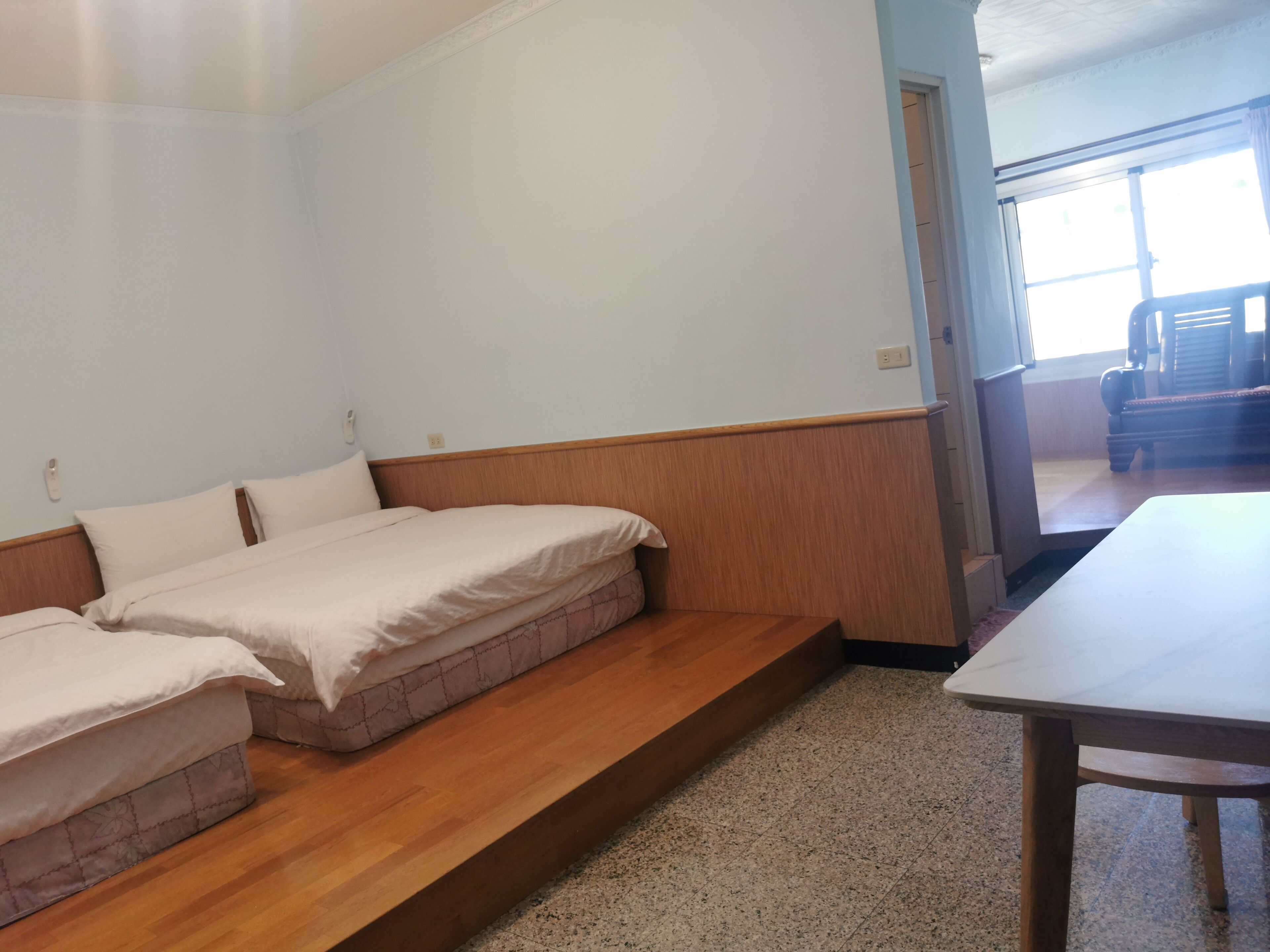 A room with two beds, a wooden bench, a table, and a window.