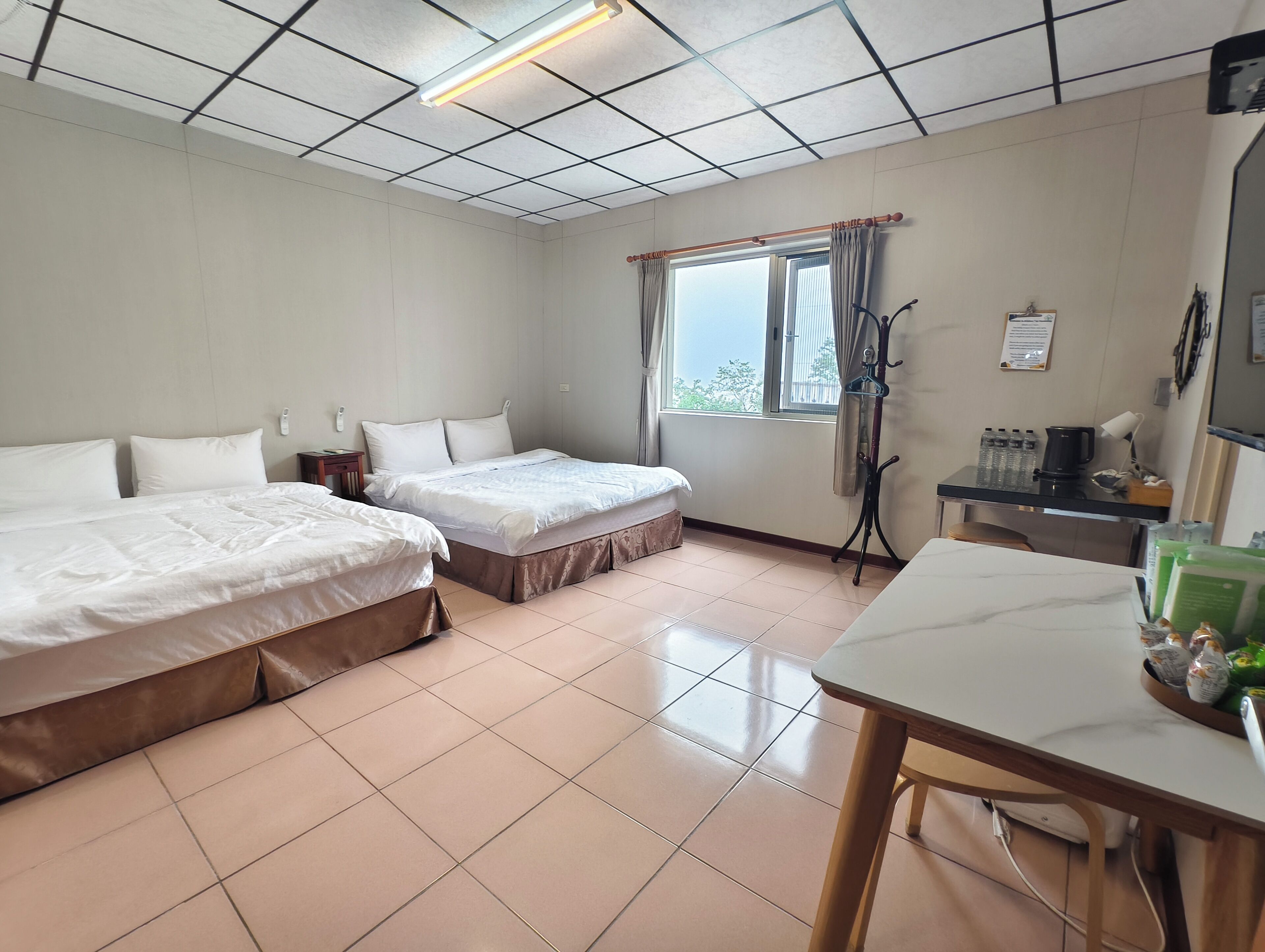 Ein Hotelzimmer mit zwei Betten, einem Schreibtisch, einem Fenster mit Vorhängen und einem Kleiderständer.