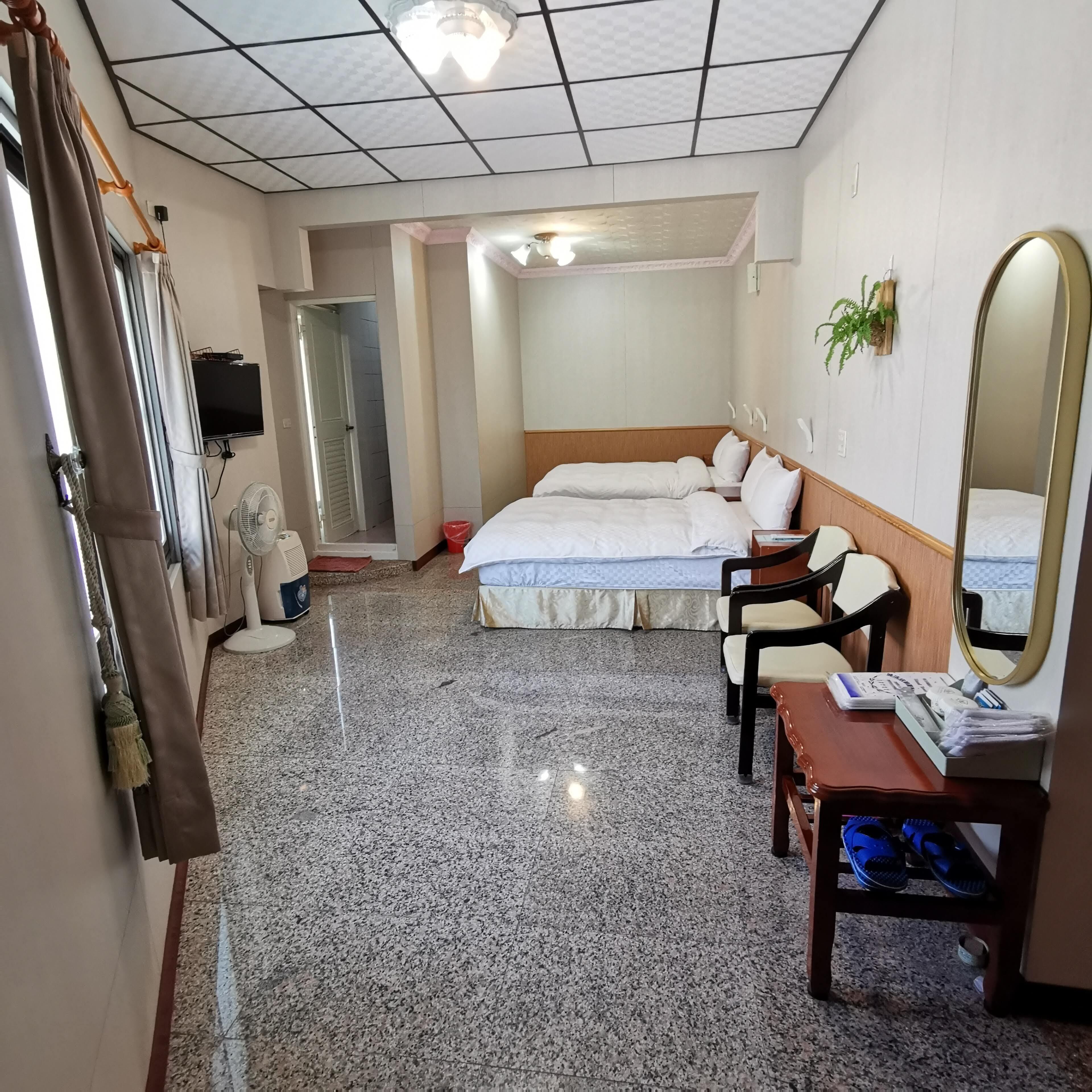 A hotel room with a bed, a desk, a chair, a mirror, and a television.