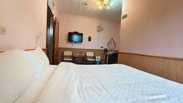 Habitación de hotel con una cama grande, televisor montado en la pared, escritorio con sillas y ventilador de techo.