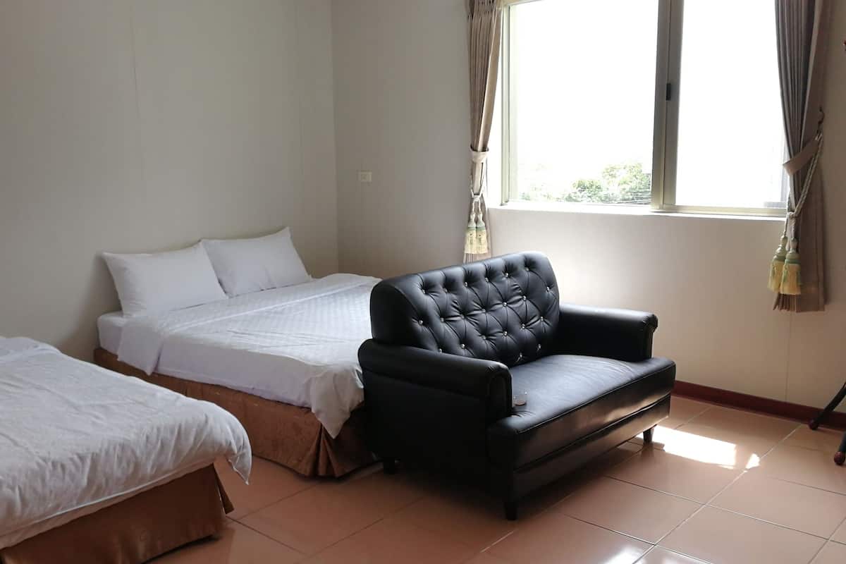 A room with two beds, a black leather sofa, and a window with curtains.