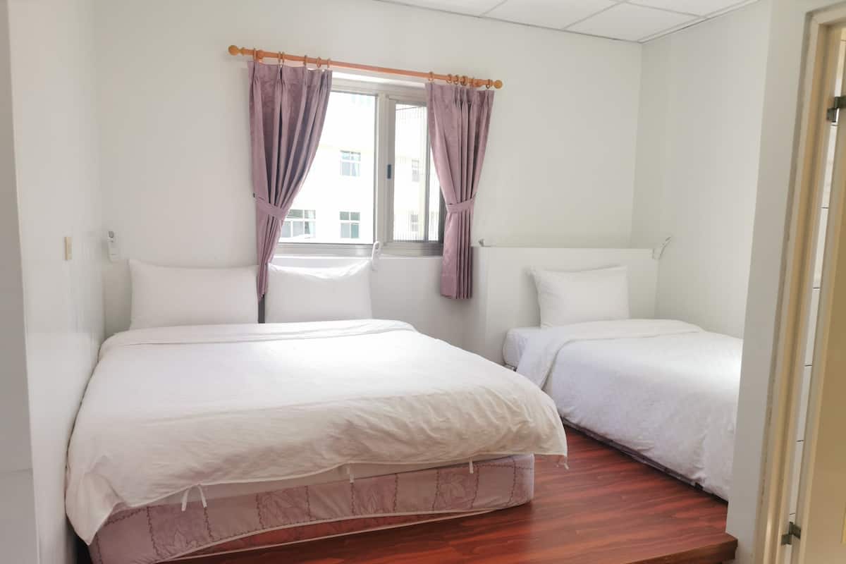 A room with two beds, a window with curtains, and a wooden floor.