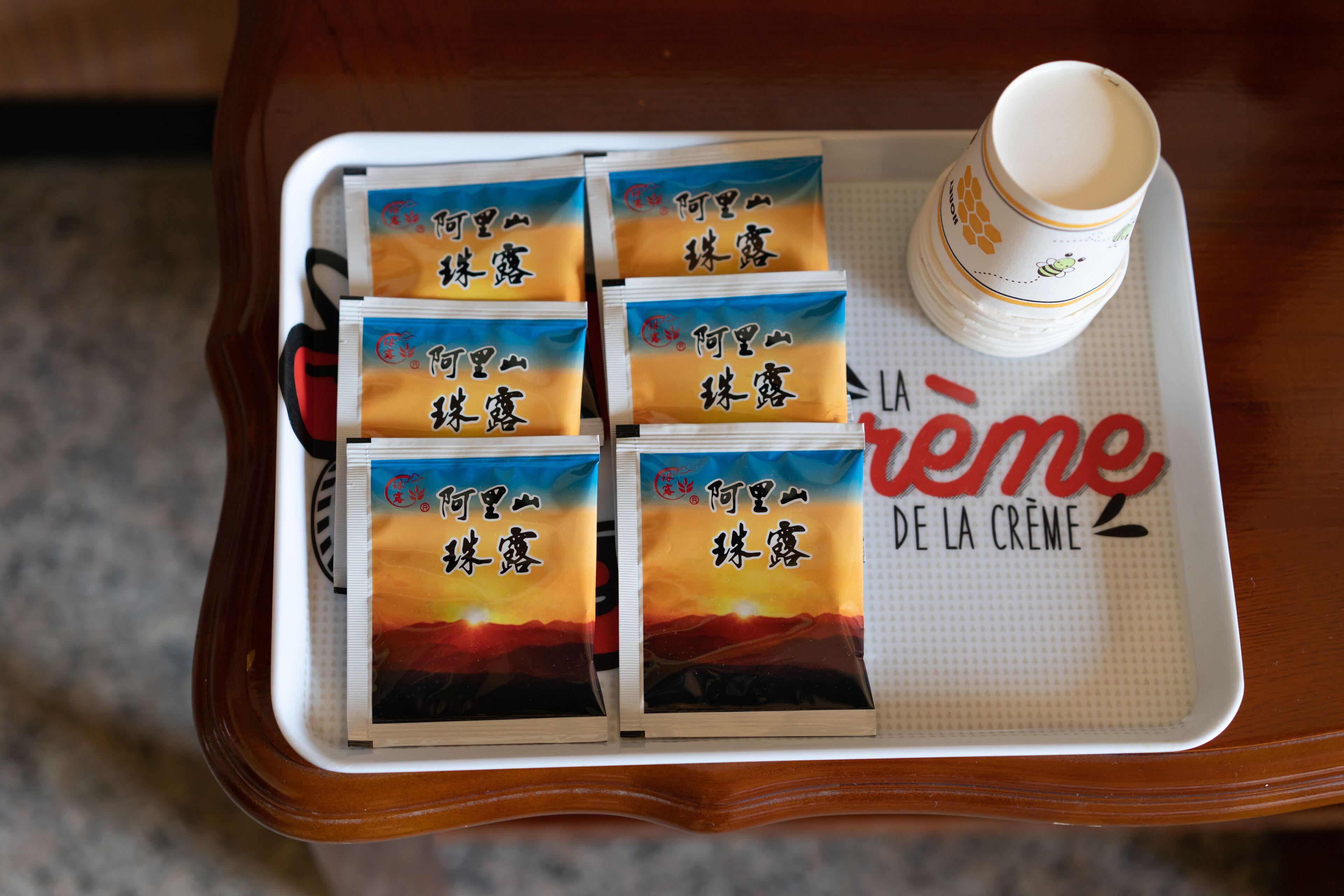 A tray with six packets of 'Artesanal de la Creme' and a cup on a wooden table.