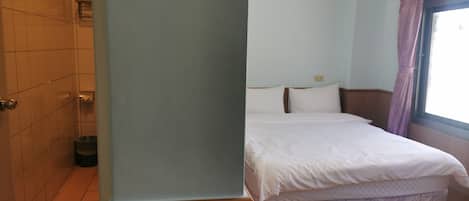 Une chambre d’hôtel avec un lit, un plancher en bois, un mur recouvert de carreaux et une fenêtre avec des rideaux.