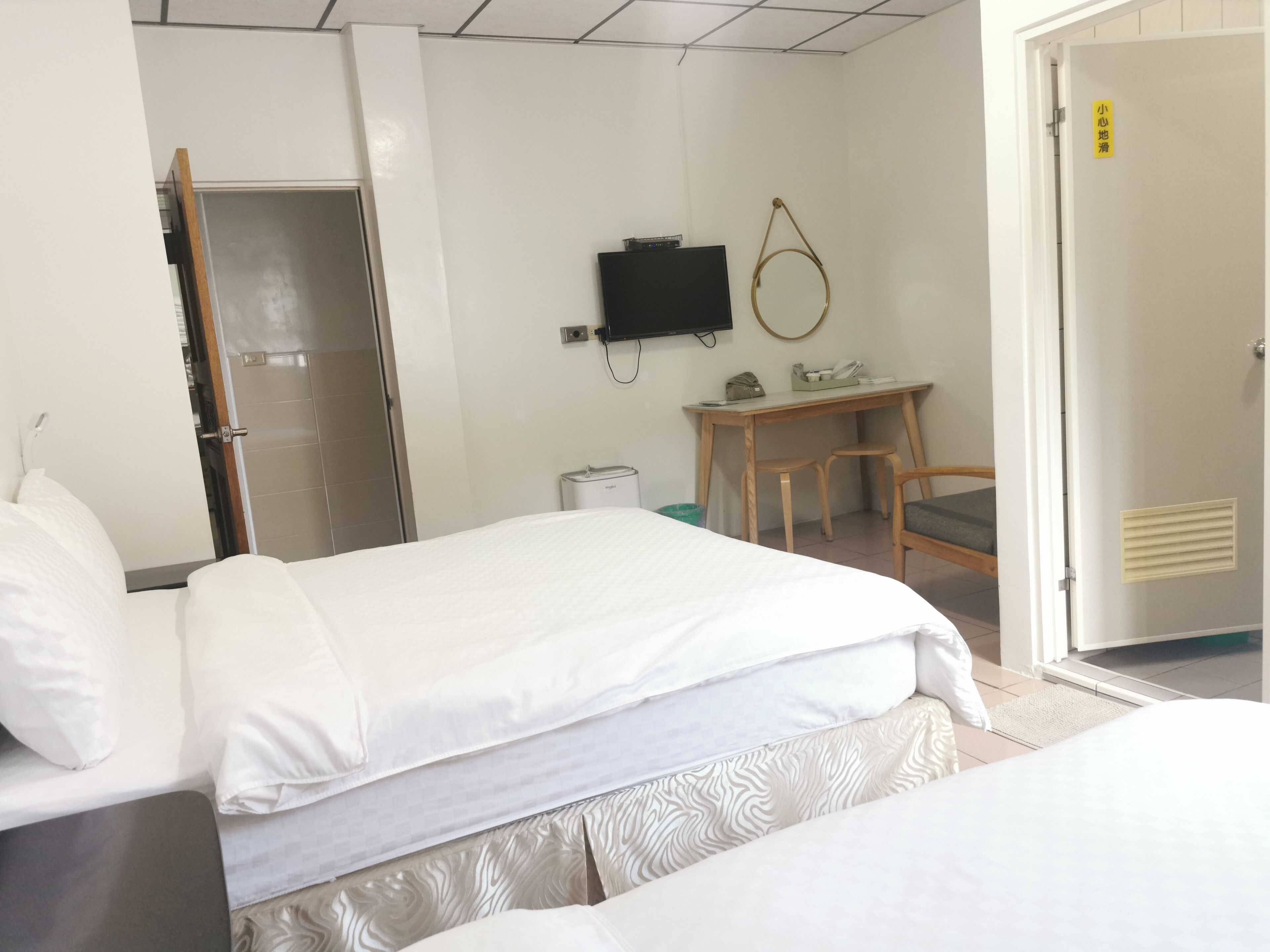 A hotel room with a bed, a desk, a chair, a television, and a door with a sign.