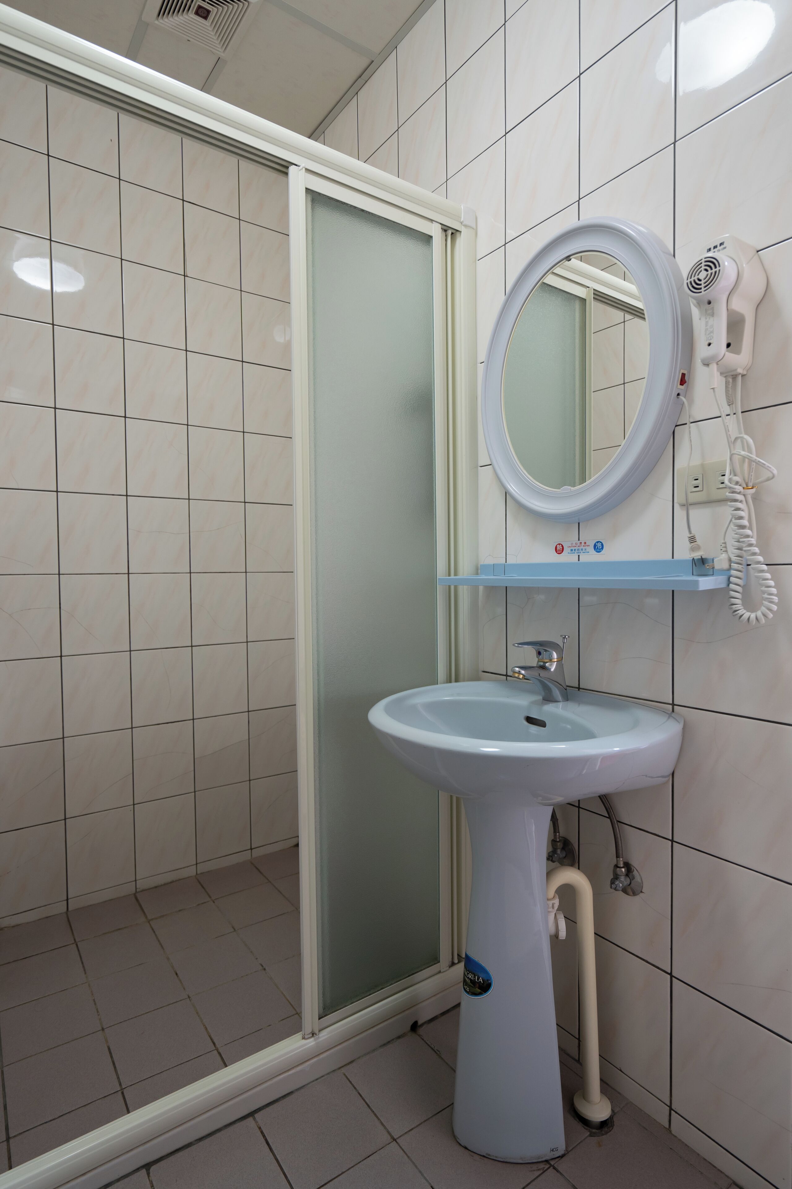A bathroom with a white sink, a mirror, and a hairdryer on a wall-mounted shelf.