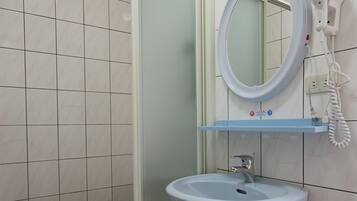 A bathroom with a white sink, a mirror, and a hairdryer on a wall-mounted shelf.