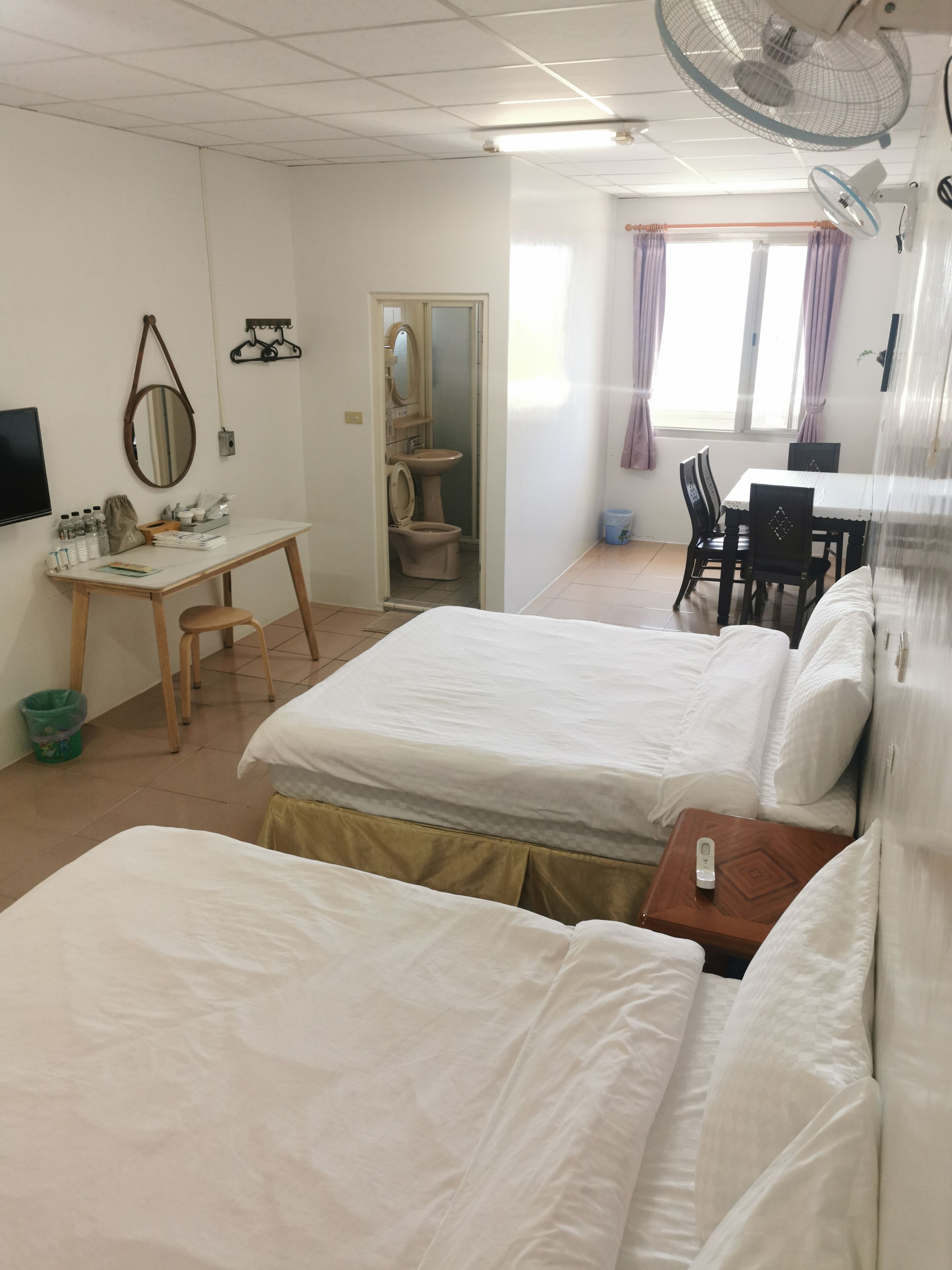 A hotel room with two beds, a desk, a chair, a table, and a bathroom.