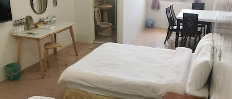 A hotel room with two beds, a desk, a chair, a table, and a bathroom.