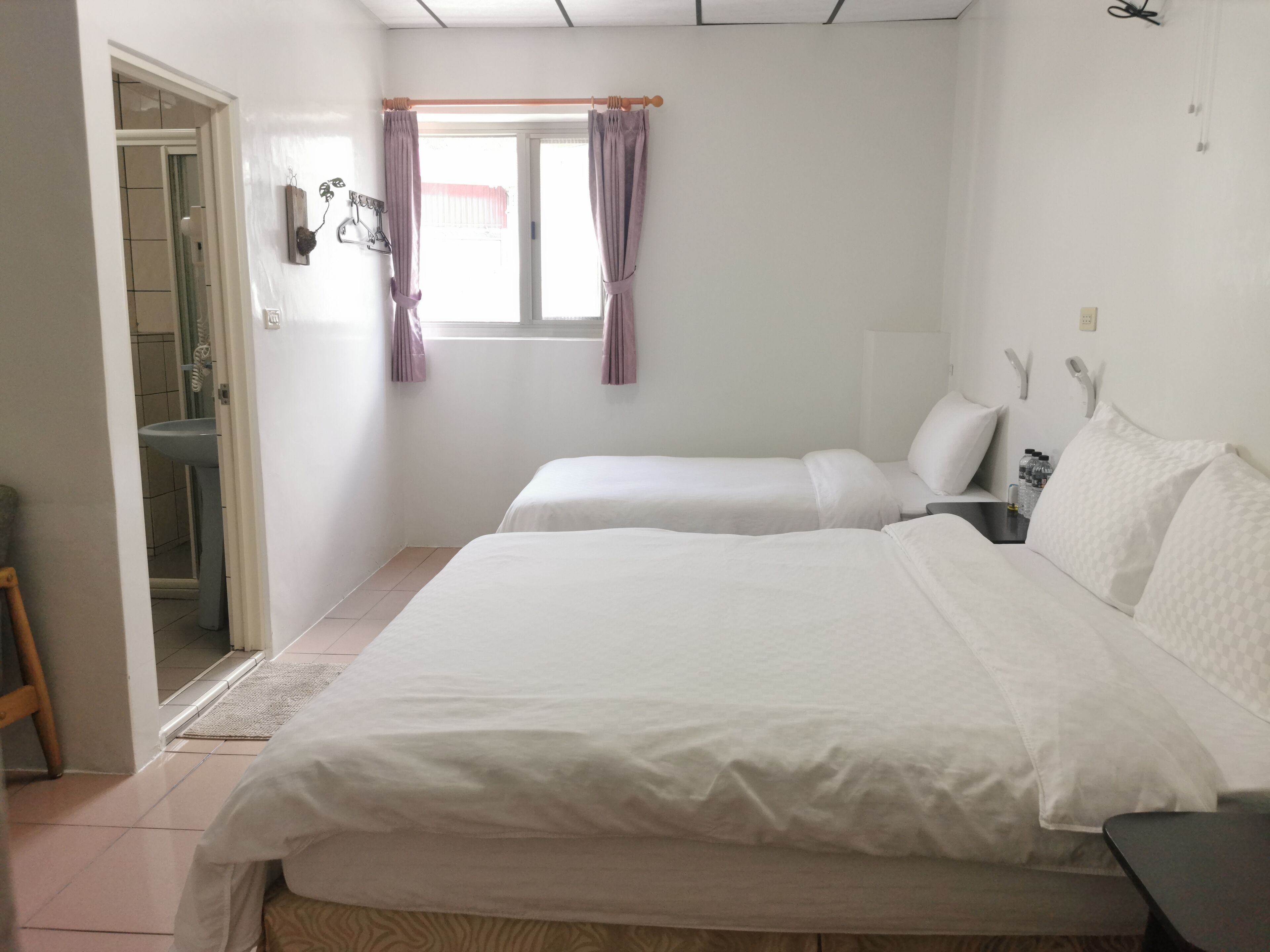 Une chambre avec deux lits, une fenêtre avec des rideaux, un lavabo et une porte donnant sur une salle de bain.
