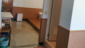 A room with a wooden bench, a small table, a trash bin, and a door leading to another room. - Alishan Tea Homestay (Alishan)