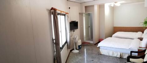 Habitación de hotel con cama, escritorio, silla, televisión, ventilador y ventana con cortinas.