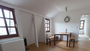 Une pièce spacieuse dotée d’un parquet en bois, d’une table à manger avec des chaises, d’un banc, d’un radiateur et d’une fenêtre offrant une vue agréable.
