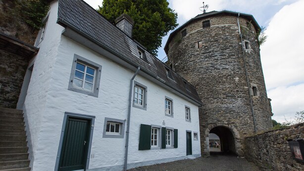 Un bâtiment historique doté d’une tour en pierre et d’une façade blanche agrémentée de volets verts.