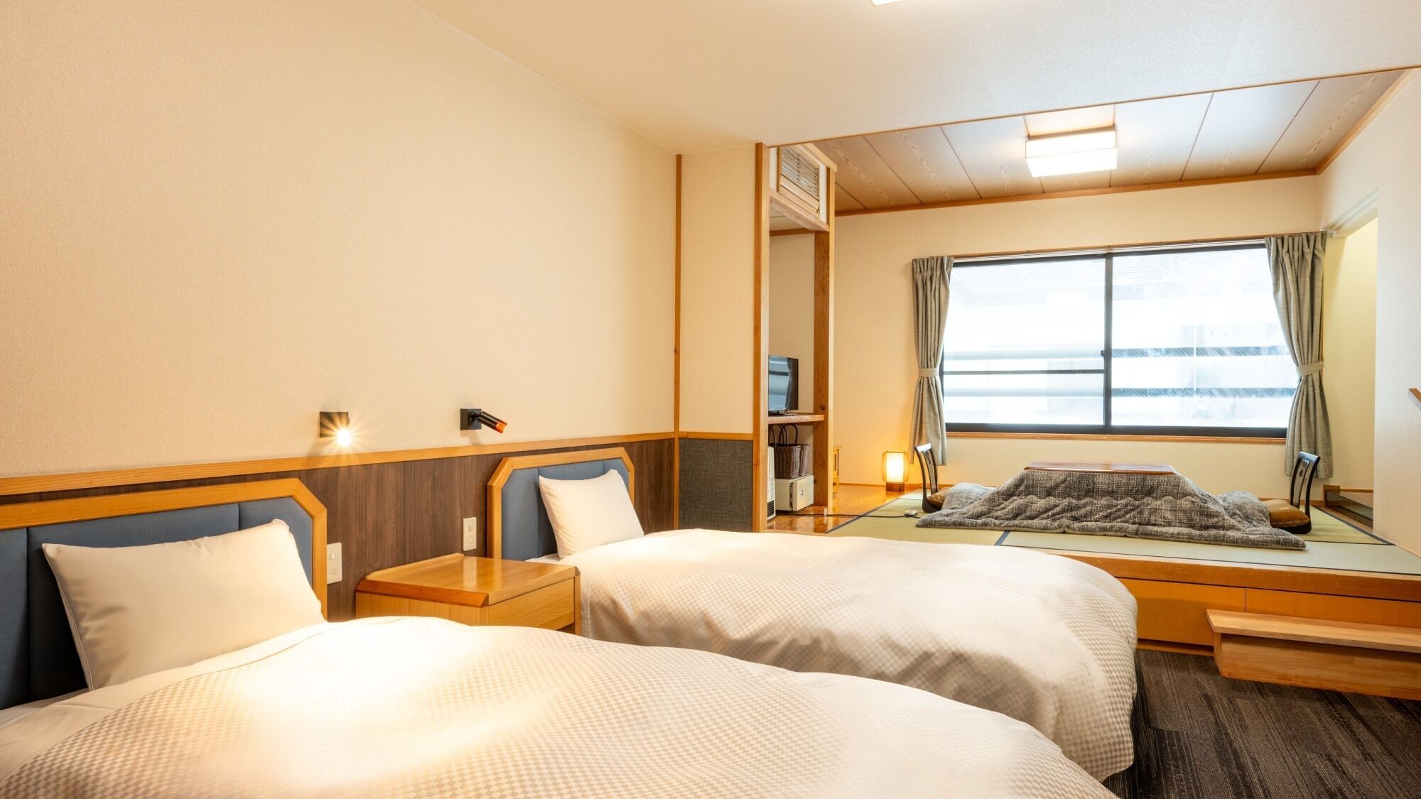 Una camera d'albergo con due letti, un'ampia finestra, una televisione e uno specchio.