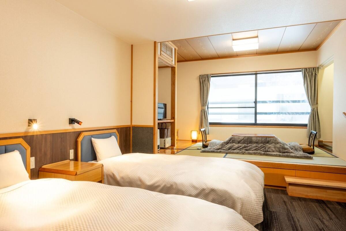A hotel room with two beds, a large window, a TV, and a mirror.