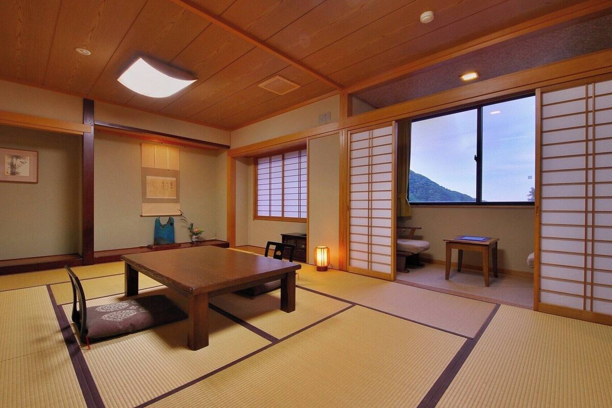 A traditional Japanese room with tatami flooring, a low table, sliding doors, and a view of a mountain.