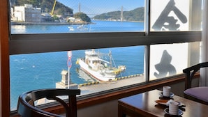 Una habitación con un ventanal grande con vistas a un puerto, una mesa con platos y dos sillas.