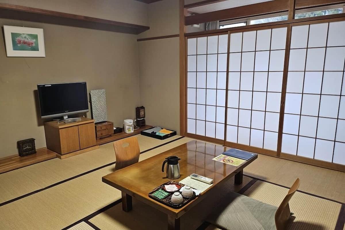 Una habitación japonesa tradicional con suelo de tatami, una mesa de madera baja, un televisor y puertas correderas shoji.