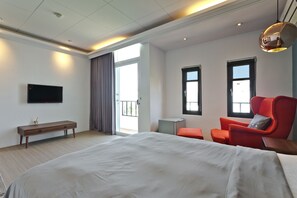 A modern hotel room with a large bed, a red armchair, a small table, and a TV mounted on the wall. - Kenting Cozy B&B (Hengchun)