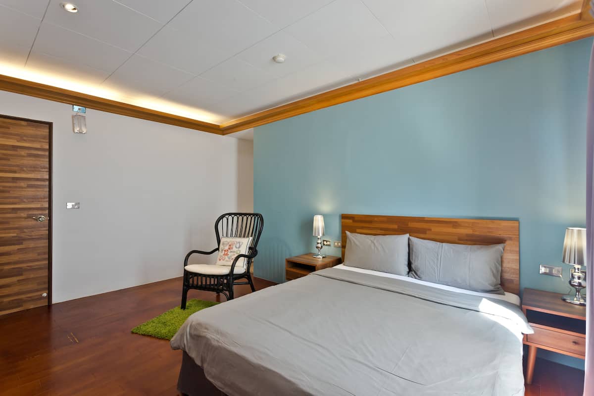 A bedroom with a bed, a chair, a nightstand, and a wooden ceiling.