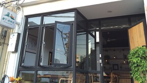 Ein modernes Gebäude mit großen Fenstern und einem Balkon. Draußen gibt es Sitzbereiche mit Stühlen und Tischen.