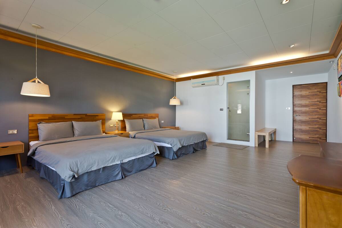 A modern hotel room with two beds, wooden flooring, and a small seating area.