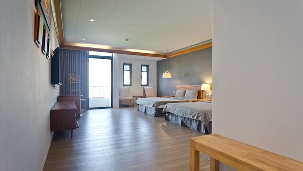 Ein Hotelzimmer mit Holzboden, zwei Betten, einem Schreibtisch, einer Bank und einem großen Fenster.