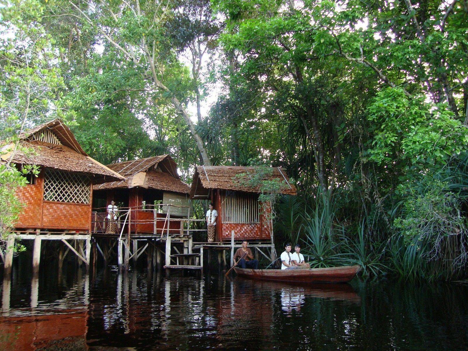 A traditional houseboat with a thatched roof, wooden railings, and a small boat docked nearby.