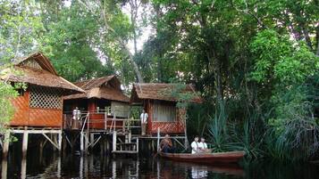 A traditional houseboat with a thatched roof, wooden railings, and a small boat docked nearby.