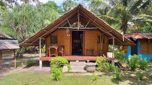 A rustic wooden house with a thatched roof, a porch with two wooden chairs, and a concrete water feature in front. - Mutiara Beach Resort (Bintan)