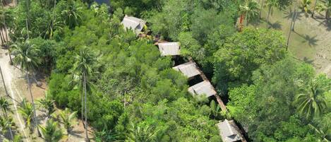 An aerial view of a remote, lush green area with a series of thatched-roof huts aligned along a narrow waterway.