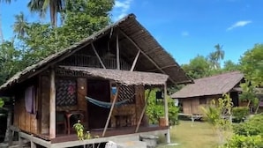 A rustic wooden house with a thatched roof, surrounded by lush greenery and palm trees. - Mutiara Beach Resort (Bintan)