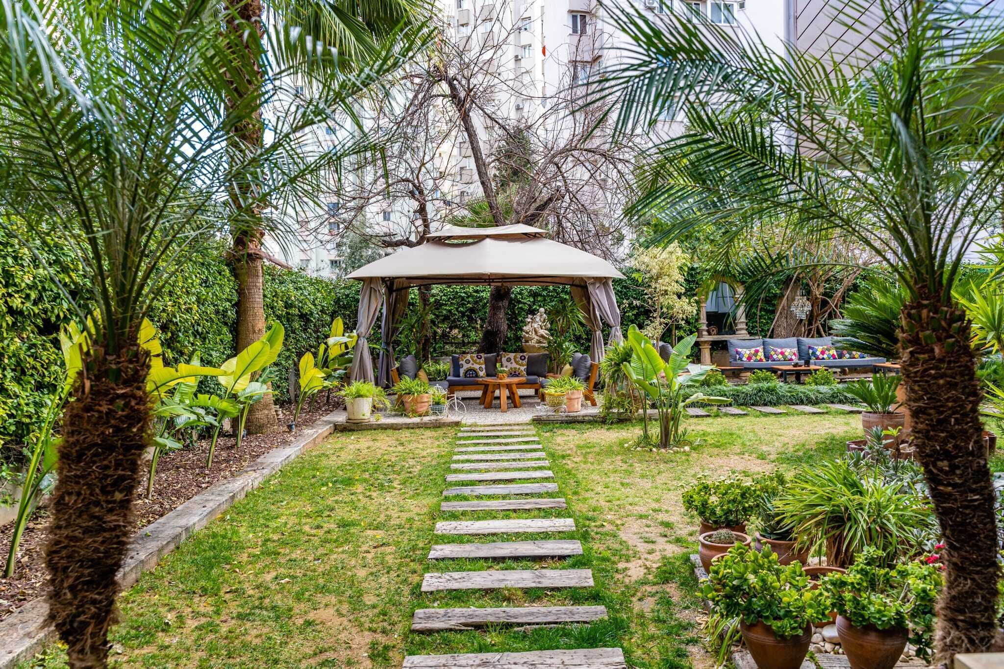 A garden with a wooden pathway leading to a gazebo with seating.