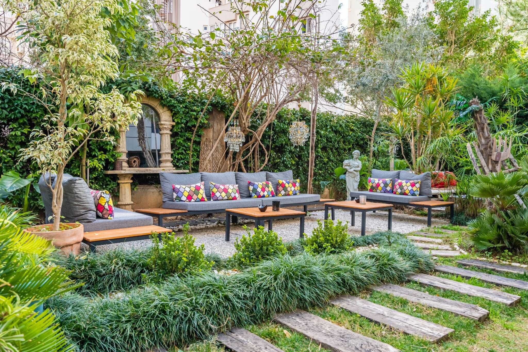 A garden patio with a sofa set, wooden tables, and a statue.