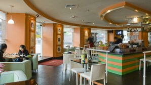 Un restaurante con techo curvo, una barra con una combinación de colores verde y naranja, y varias mesas y sillas.