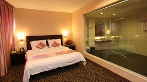 Una habitación de hotel con una cama grande, una mesita de noche con teléfono, zona de ducha con mampara de vidrio y alfombra estampada.
