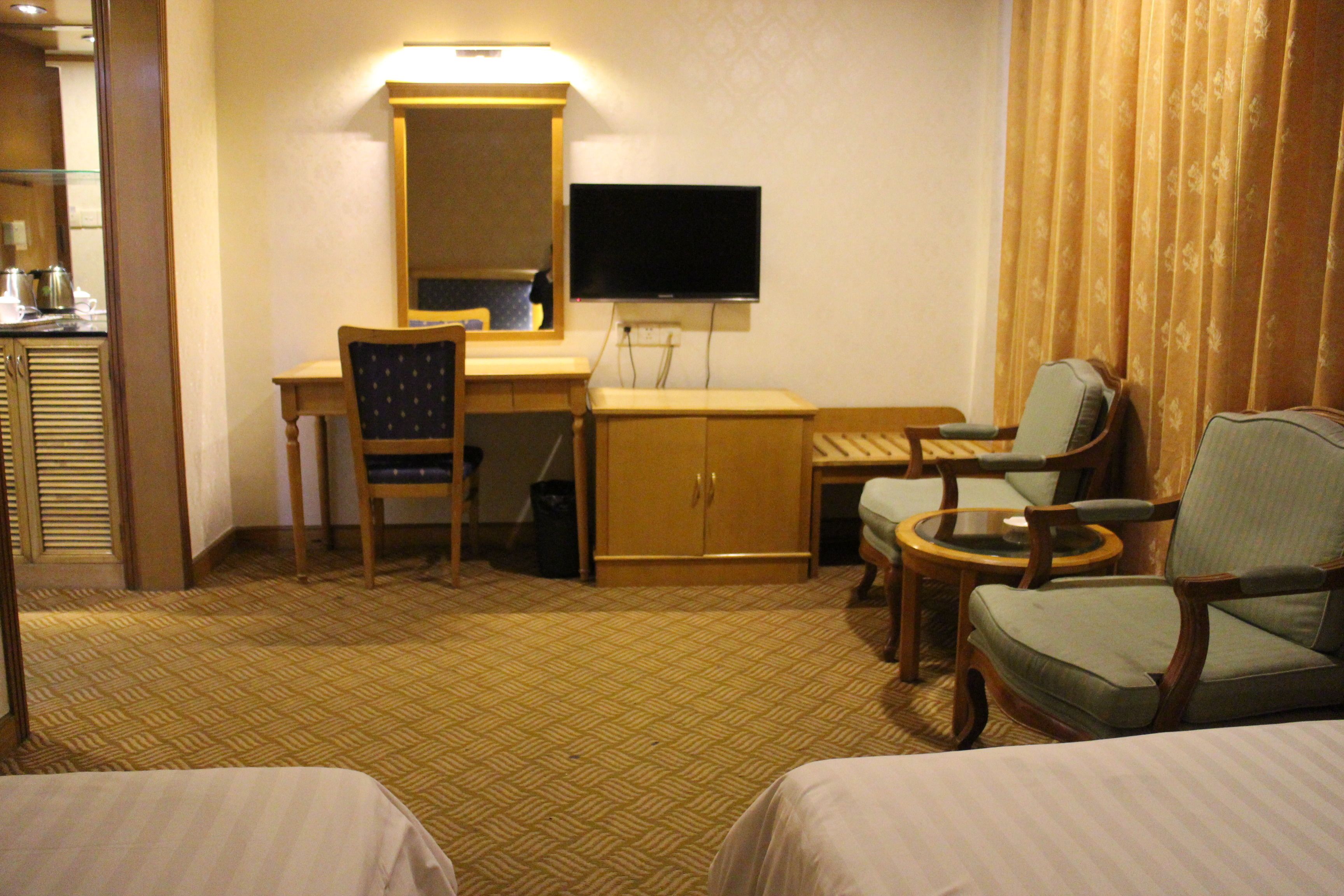 Una camera d'hotel con un letto, due poltrone, una scrivania con una sedia, una televisione e un armadio.
