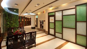 Vestíbulo de hotel con mostrador de recepción, zona de estar y una escalera que lleva a un ascensor.