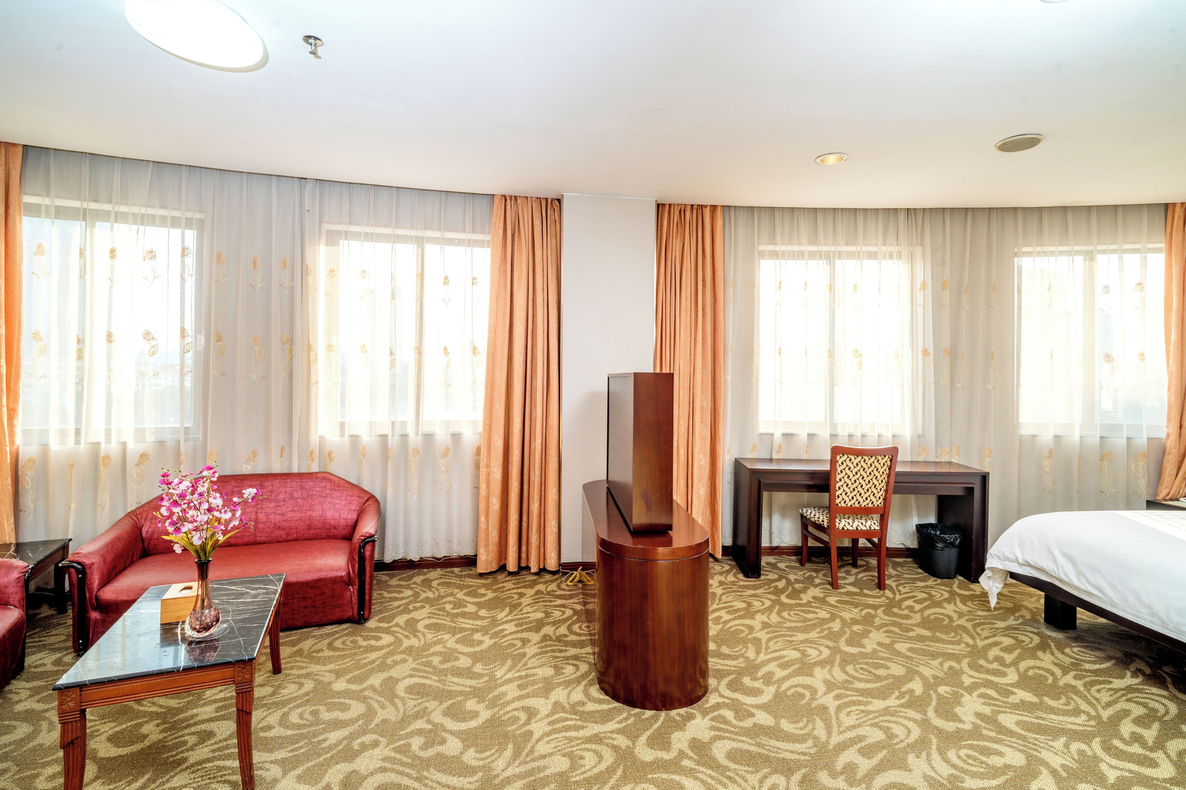 Habitación de hotel con sofá, cama, escritorio, silla, televisor y un florero con flores.