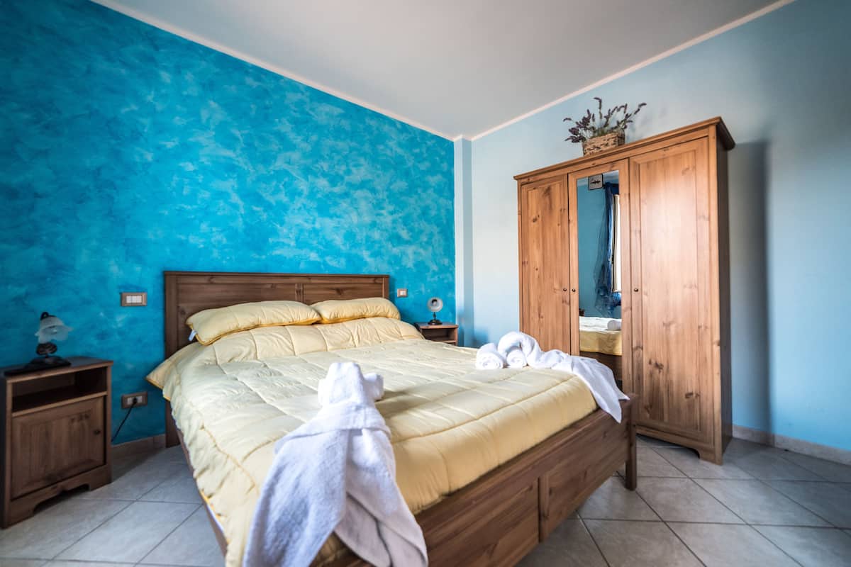 A bedroom with a bed, wooden wardrobe, and a nightstand.
