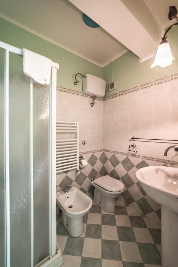 Un baño con suelo a cuadros, un bidé, un inodoro, un lavamanos y una ducha con puerta de cristal.