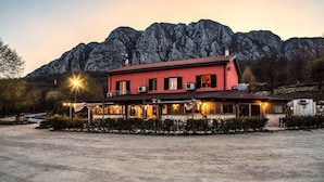 A two-story building with a red facade and multiple windows, situated in a rural area with a mountain backdrop. - Locanda Belvedere (Rocchetta a Volturno)