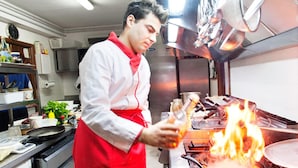 A chef in a kitchen with a stove and a pan on fire. - Locanda Belvedere (Rocchetta a Volturno)