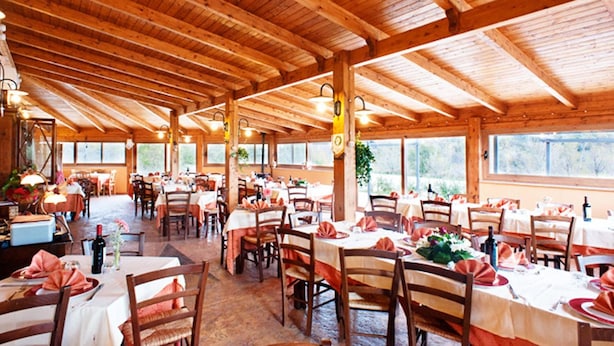 A spacious restaurant with wooden beams and large windows. Tables are set with white tablecloths and red napkins. - Locanda Belvedere (Rocchetta a Volturno)