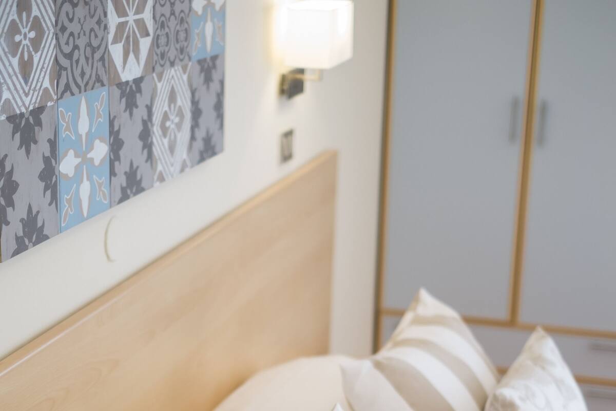 Una cama bien hecha con almohadas a rayas y estampadas, un cabecero de madera y una pared con azulejos decorativos.
