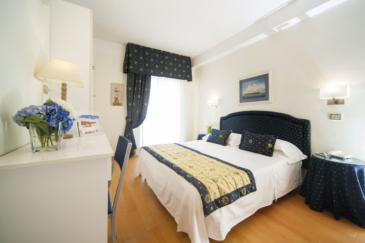 Una habitación de hotel con cama, mesita de noche, lámpara y un jarrón con flores.