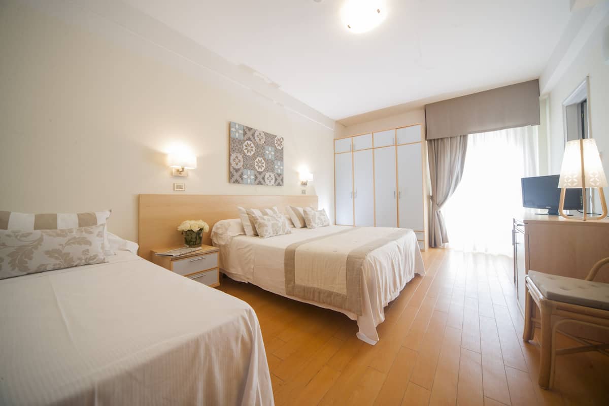 Una habitación de hotel con dos camas, un escritorio, una silla, un televisor y un ventanal con cortinas.