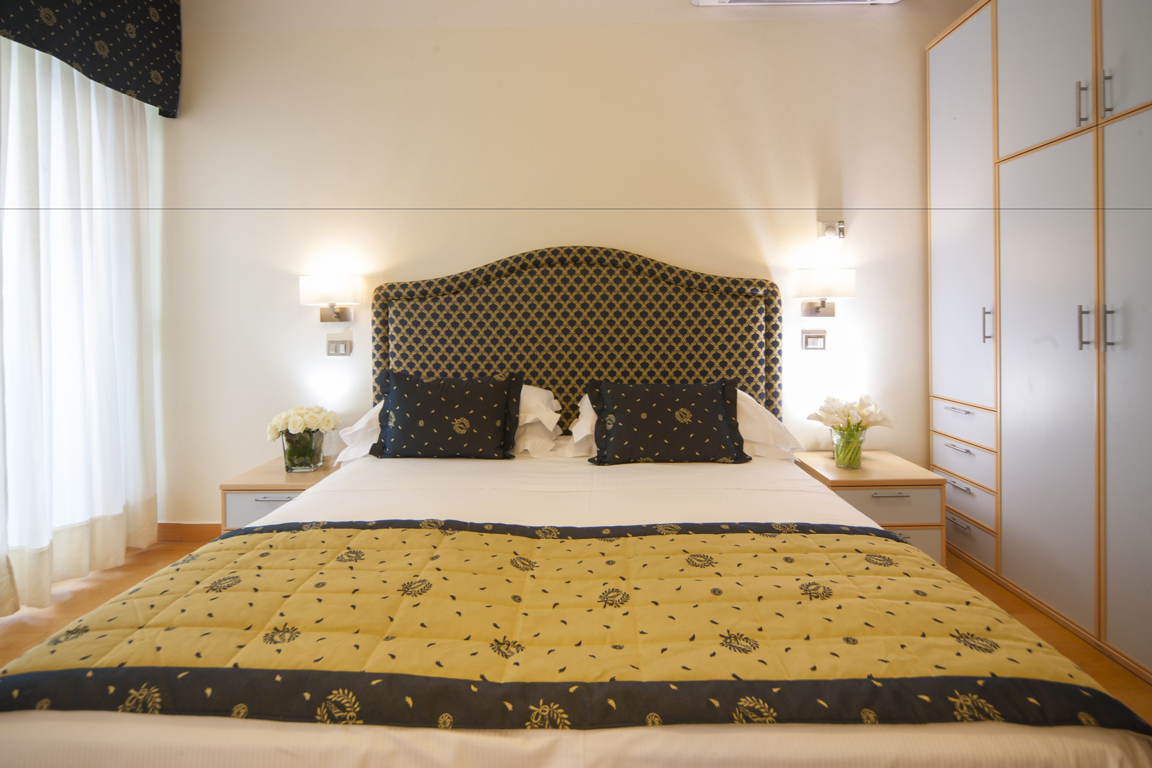 Une chambre à coucher bien rangée, avec un grand lit, deux tables de chevet avec des lampes, une armoire et une fenêtre avec des rideaux.