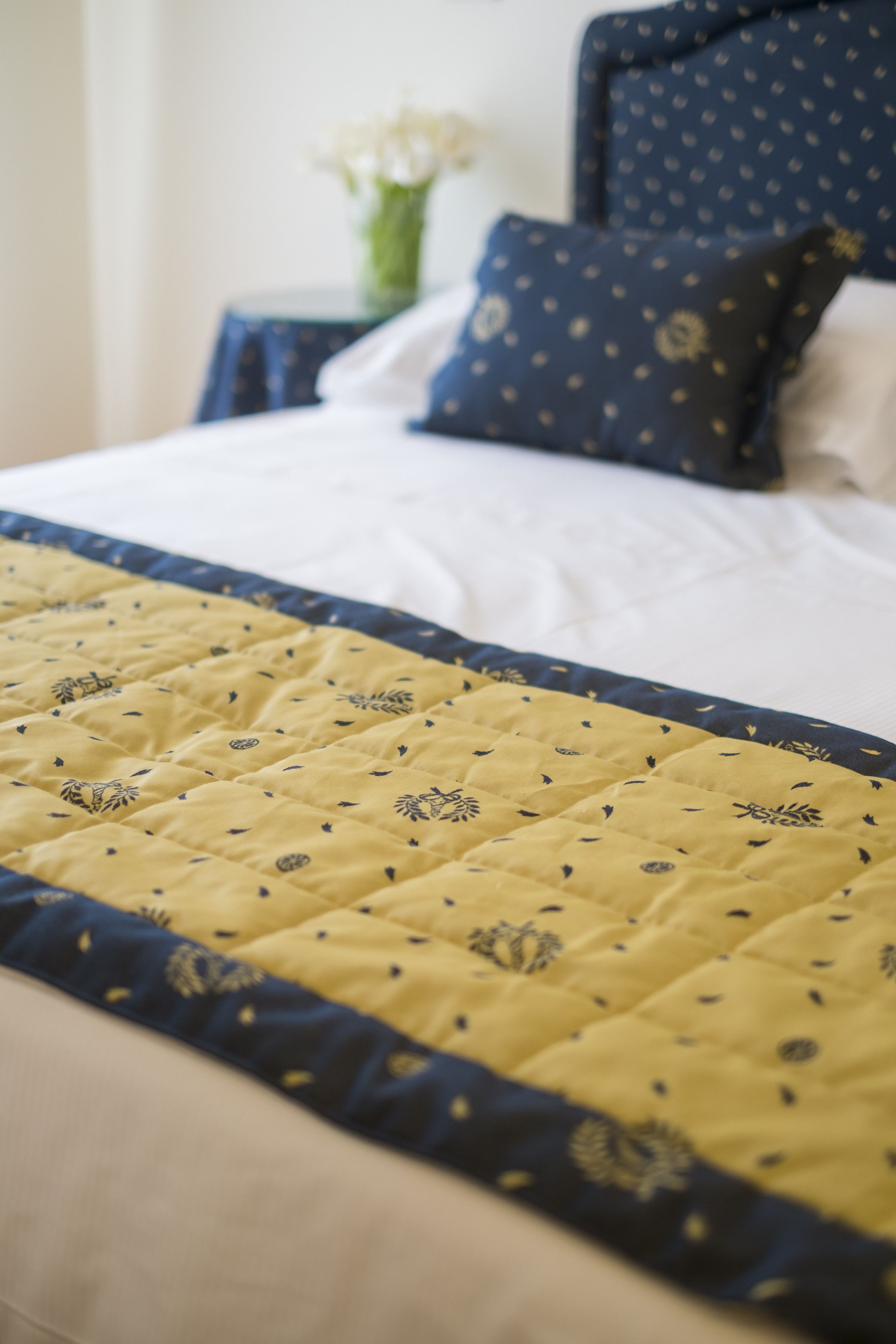A bed with a yellow quilt and a dark blue headboard.